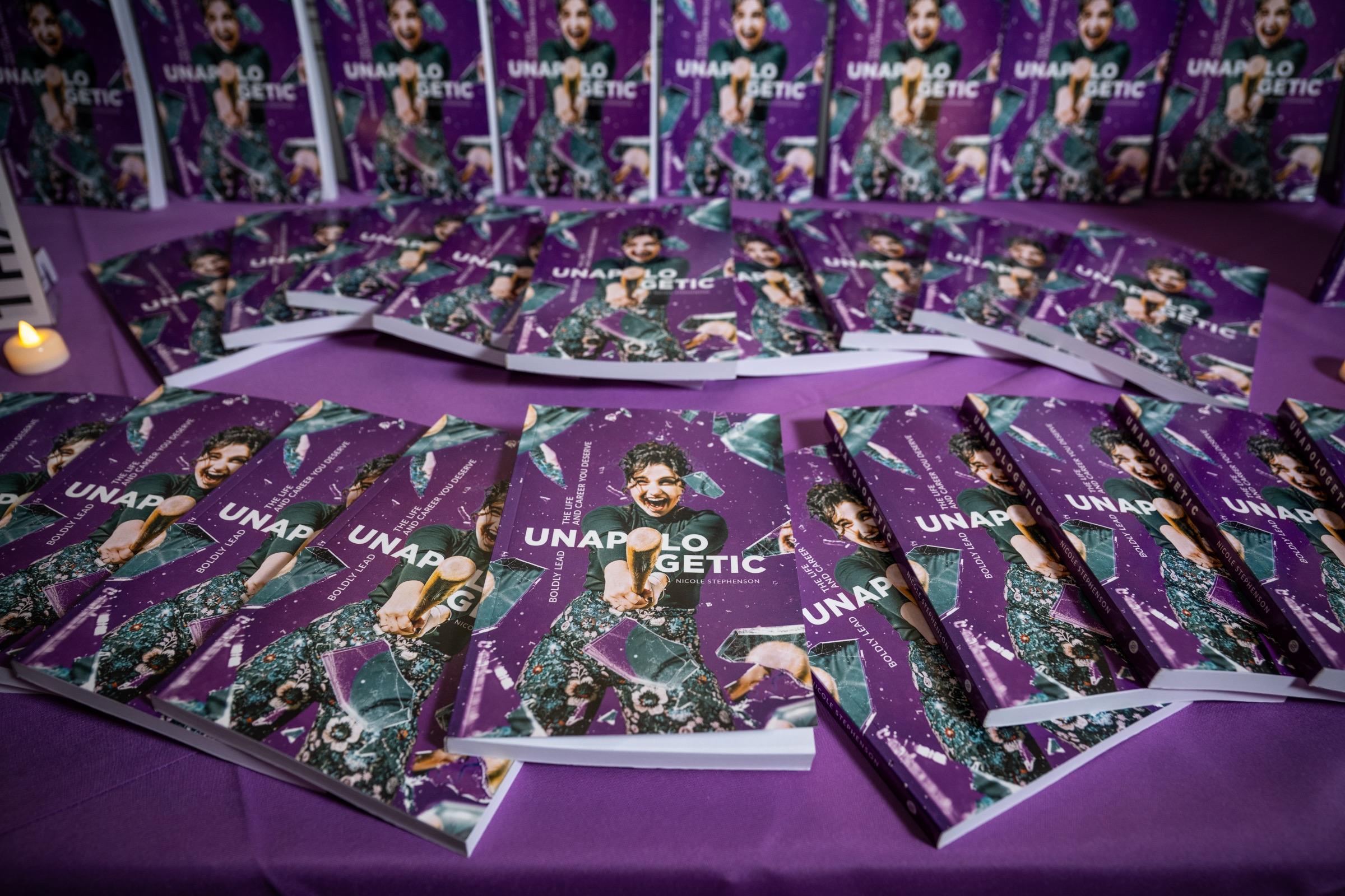 Stacks of Unapologetic copies on a purple-draped table at the book launch.